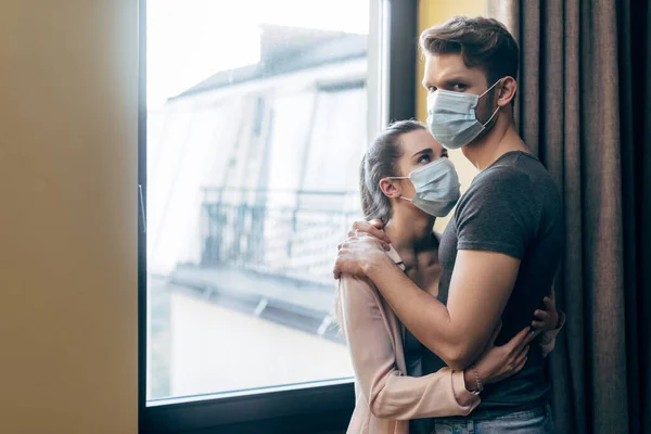 Mujer en máscara médica abrazando novio en casa - foto de stock