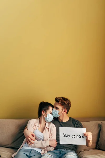 Чоловік обіймає дівчину в медичній масці і тримає плакат з листом додому — стокове фото