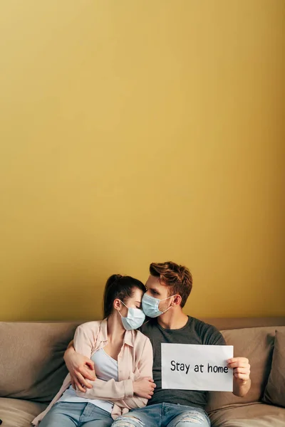 Man hugging girl in medical mask and holding placard with stay home lettering — Stock Photo