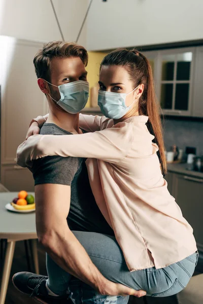 Мужчина в медицинской маске держит в руках девушку и смотрит в камеру — стоковое фото