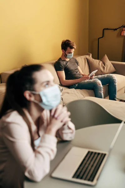 Selective focus of man in medical mask using digital tablet while freelancer with clenched hands sitting near laptop — Stock Photo