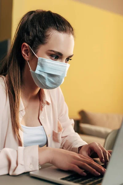 Selective focus of freelancer in medical mask using laptop at home — Stock Photo
