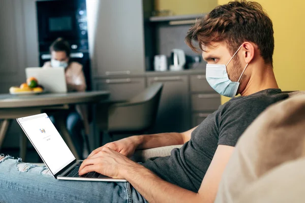 KYIV, UKRAINE - APRIL 22, 2020: selective focus of freelancer in medical mask using laptop with google website near girl — стокове фото