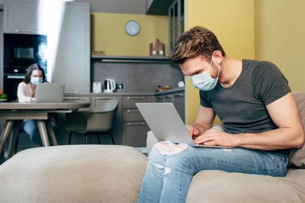 Selektiver Fokus der Freiberuflerin in medizinischer Maske, die von zu Hause aus in der Nähe ihrer Freundin arbeitet — Stockfoto