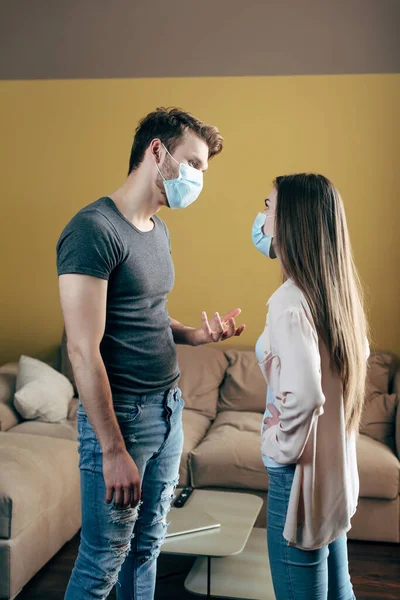 Man in medical mask gesturing while quarreling with girlfriend at home — Stock Photo