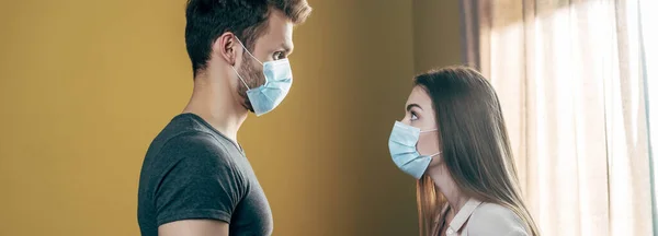 Plan panoramique de couple en masques médicaux se querellant à la maison — Photo de stock