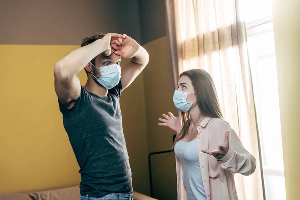 Woman in medical mask gesturing while quarreling with boyfriend at home — Stock Photo