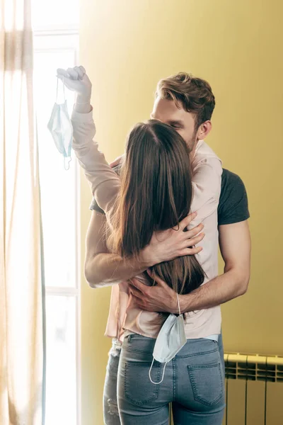 Hombre abrazando novia con máscara médica en la mano, fin del concepto de cuarentena - foto de stock