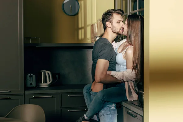 Bearded man kissing seductive girl in kitchen — Stock Photo