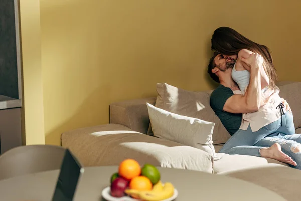 Selective focus of sexy couple kissing on sofa near fruits on table — Stock Photo