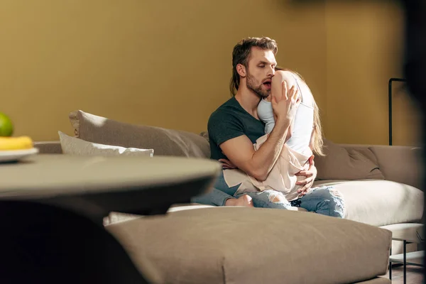 Selektiver Fokus eines bärtigen Mannes, der Freundin auf Sofa küsst — Stockfoto