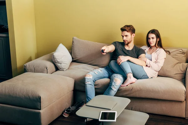 Bearded man watching movie near girlfriend, laptop and digital tablet with blank screen on coffee table — Stock Photo