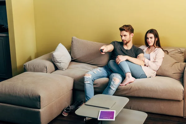 KYIV, UKRAINE - 22 de abril de 2020: Homem barbudo assistindo filme perto de namorada, laptop e tablet digital com aplicativo instagram na mesa de café — Fotografia de Stock