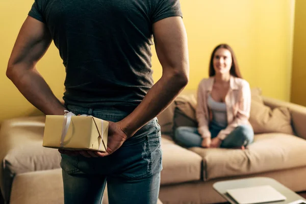 Selective focus of man holding present behind back near girlfriend in living room — Stock Photo