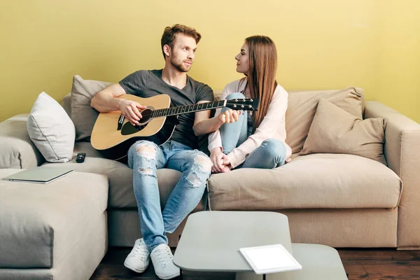 Guapo hombre tocando la guitarra acústica cerca de atractiva chica y tableta digital con pantalla blanca - foto de stock