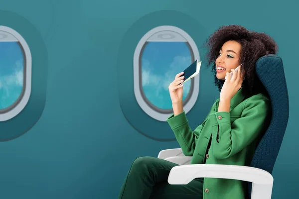 Smiling african american woman talking on smartphone and holding passport with air ticket on green background with portholes — Stock Photo