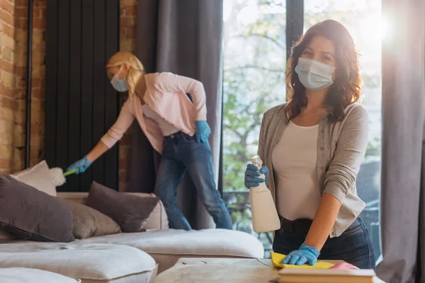 Selective focus of woman in medical mask cleaning table while kid using dust brush at home — Stock Photo