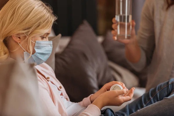 Selective focus of child in medical mask holding jar with pills near mother with glass of water — Stock Photo