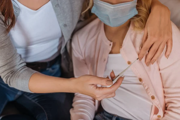 Vista recortada de la madre sosteniendo el termómetro cerca del niño en máscara médica - foto de stock