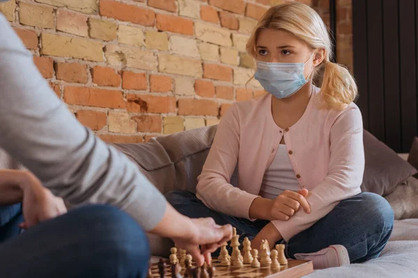 Selective focus of kid in medical mask playing chess with mother at home — Stock Photo