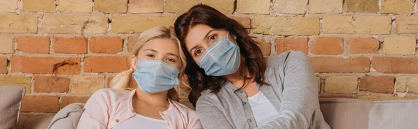Mother and daughter in medical masks looking at camera at home — Stock Photo