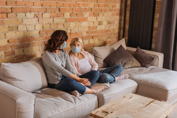 Mutter und Tochter in Arztmasken schauen sich auf Couch im Wohnzimmer an — Stockfoto