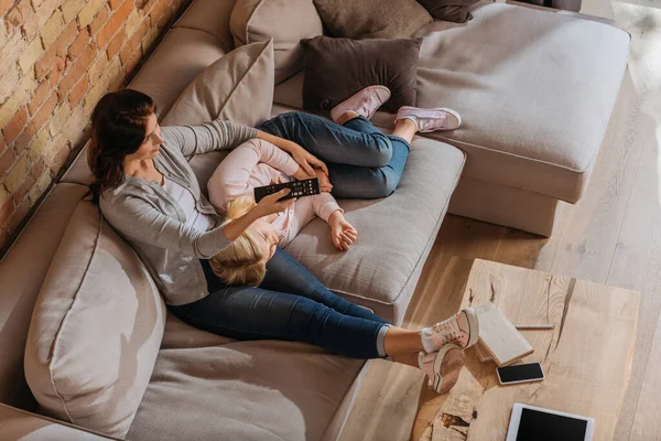 Ansicht der Mutter, die Kanäle anklickt, in der Nähe eines Kindes, das auf der Couch liegt — Stockfoto