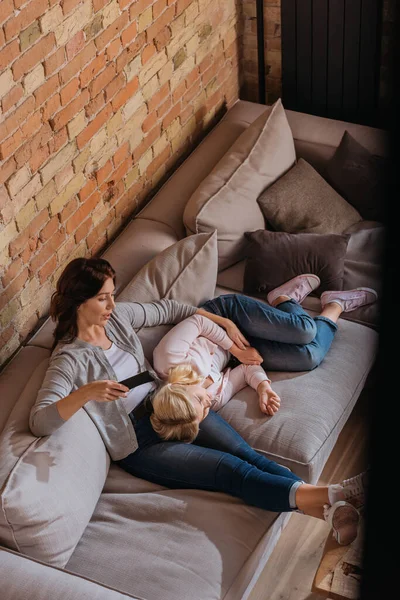 High angle view of mother and daughter watching tv on couch in living room — Stock Photo