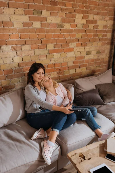 Mãe abraçando criança enquanto segurando controlador remoto no sofá — Fotografia de Stock