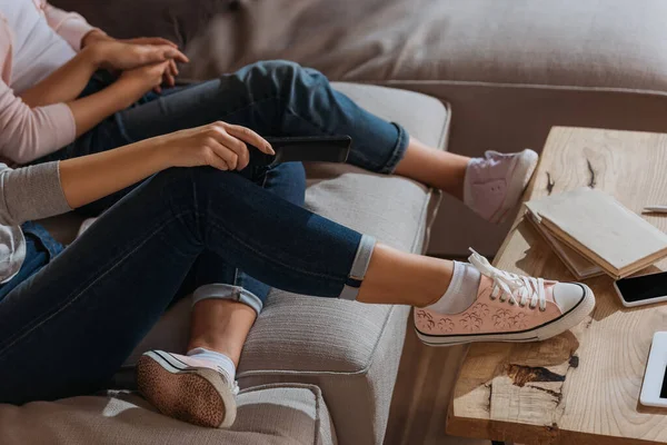 Vista recortada de la madre sosteniendo el mando a distancia cerca del niño en el sofá en casa - foto de stock