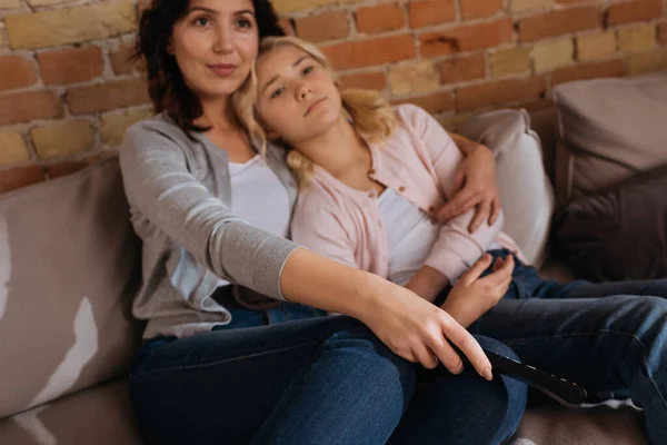 Selective focus of woman holding remote controller and hugging child on couch — Stock Photo