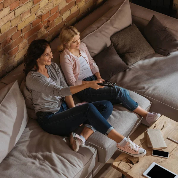 Visão aérea de mãe sorridente e filha assistindo tv perto de gadgets na mesa de café — Fotografia de Stock