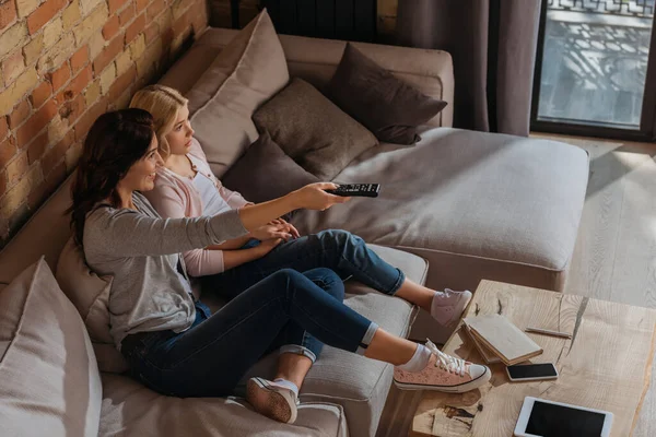 High angle view of smiling woman using remote controller near daughter on couch — Stock Photo