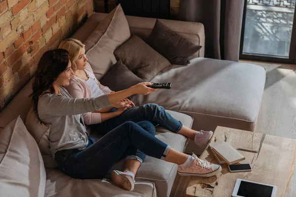 Vista ad alto angolo di donna sorridente utilizzando telecomando vicino figlia sul divano — Foto stock