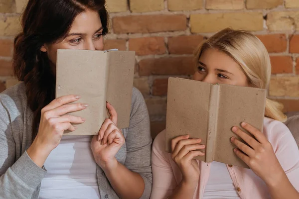 Мати і дочка вкривають обличчя книгами вдома — стокове фото