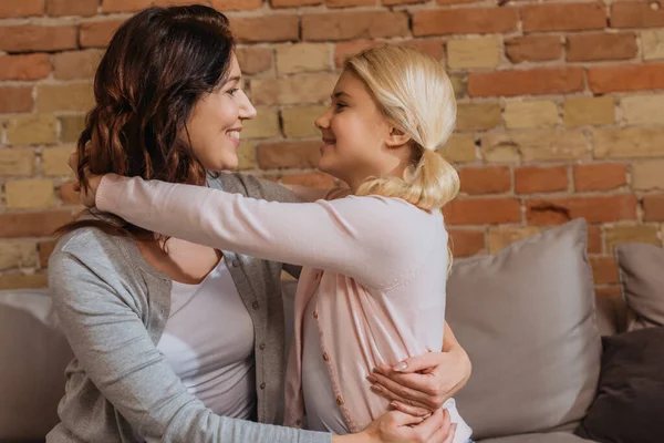 Mutter und Kind lächeln einander an, während sie sich auf der Couch umarmen — Stockfoto