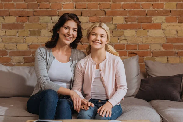 Lächelndes Kind mit Mutter, die zu Hause auf dem Sofa in die Kamera schaut — Stockfoto
