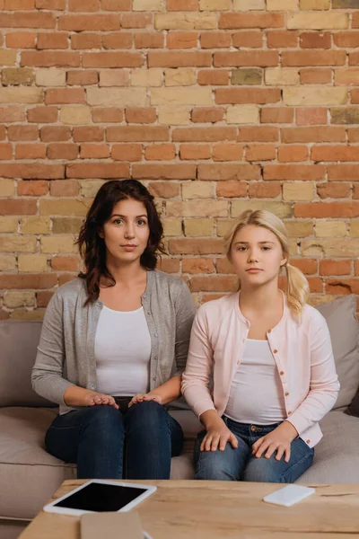 Mother and child looking at camera while sitting on sofa in living room — Stock Photo