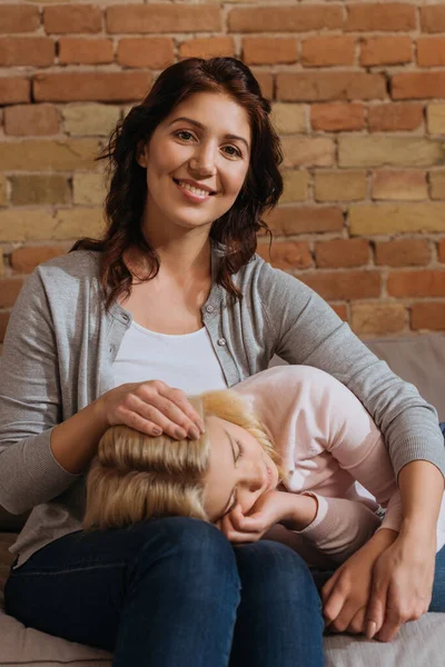 Lächelnde Mutter blickt in die Kamera, während Tochter auf Couch liegt — Stockfoto