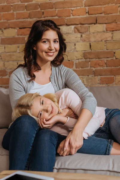 Selective focus of smiling mother and daughter looking at camera on sofa at home — Stock Photo