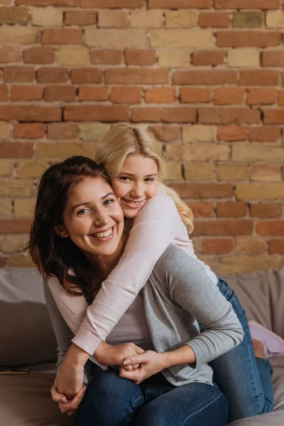 Lächelndes Kind umarmt glückliche Mutter und blickt auf Couch in die Kamera — Stockfoto