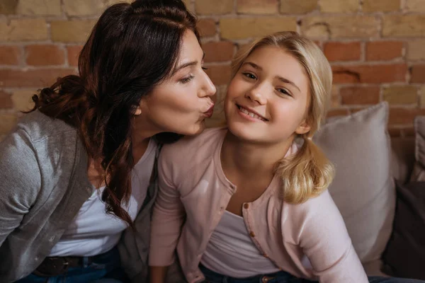 Mãe beijando garoto sorrindo olhando para a câmera no sofá — Fotografia de Stock