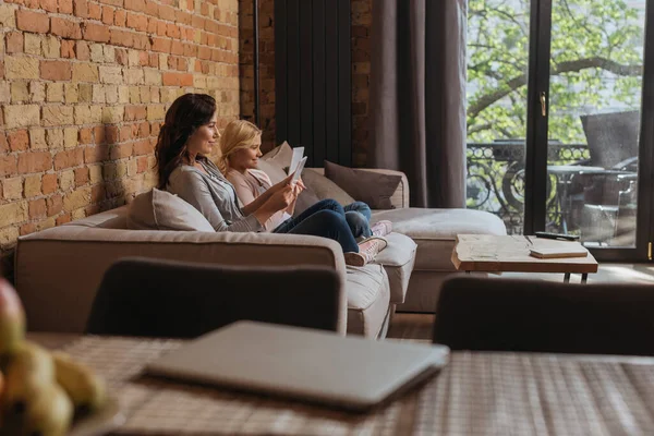 Selective focus of smiling mother and kid using digital tablets on couch in living room — Stock Photo