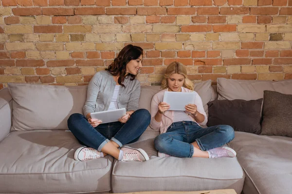 Sonriente madre sentada cerca de su hija usando tableta digital en el sofá — Stock Photo