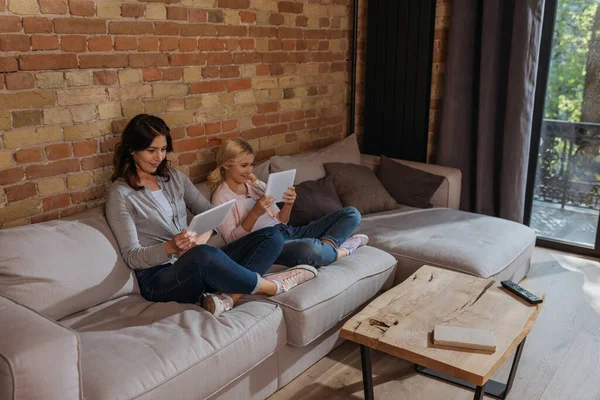 Mutter und lächelndes Kind mit digitalen Tablets auf dem heimischen Sofa — Stockfoto