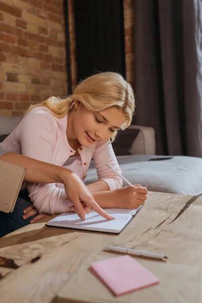 Selective focus of mother pointing with finger at notebook near smiling daughter holding pencil — Stock Photo