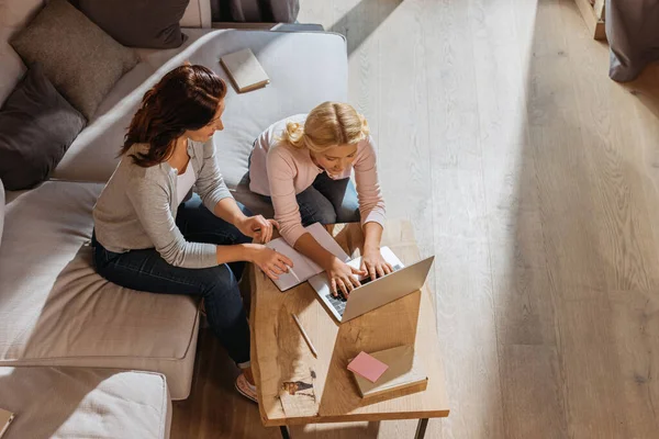 Overhead view of mother sitting near daughter using laptop during online learning at home — Stock Photo