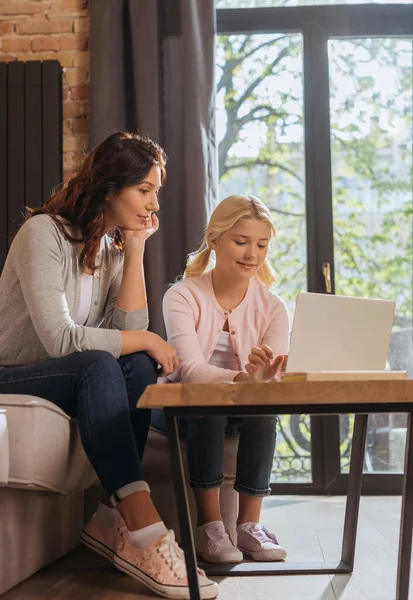 Mutter sitzt neben lächelndem Kind mit Laptop im Wohnzimmer — Stockfoto