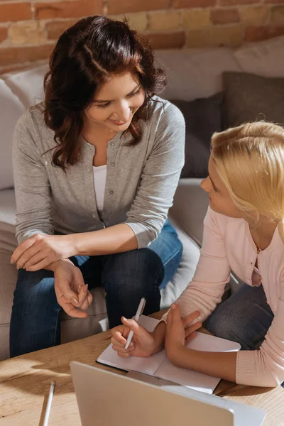 Selektiver Fokus einer lächelnden Mutter, die ihr Kind mit Stift in der Nähe von Notizbuch und Laptop zu Hause betrachtet — Stockfoto