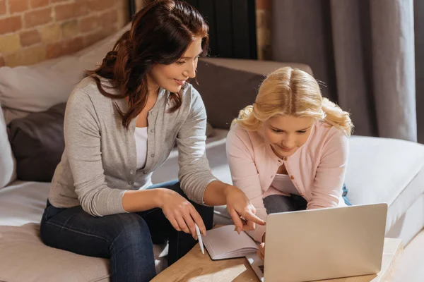 Lächelnde Mutter zeigt bei Online-Schulung auf Laptop in der Nähe der Tochter — Stockfoto